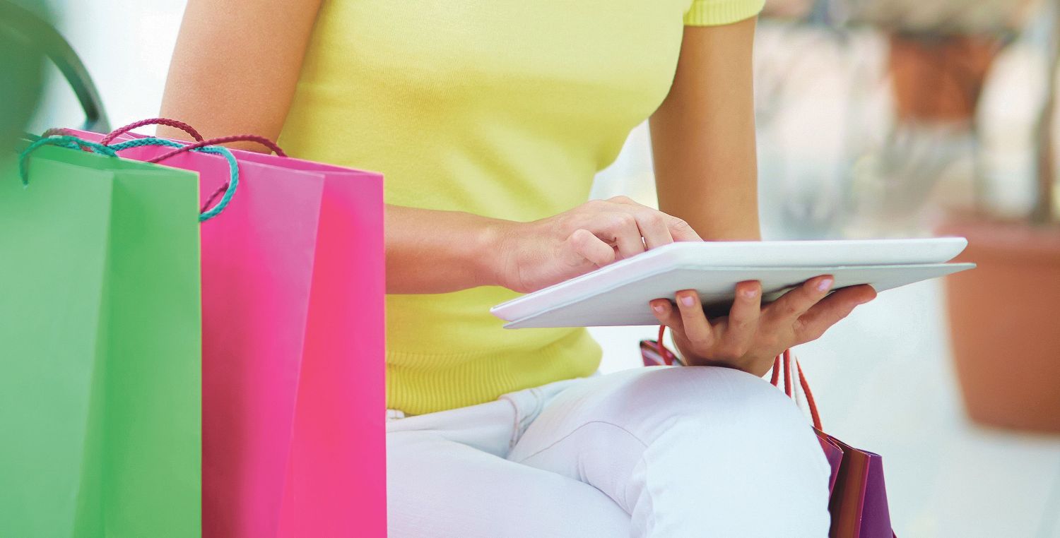 Frau mit Tablet sitzt neben Shopping-Tüten. Thema: Geschäftsmodelle